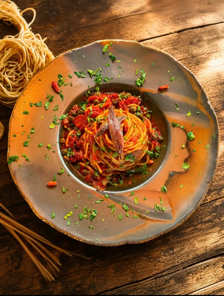 Spaghetti alla puttanesca podane w O Sole Mio Italiano — makaron z sosem z pomidorów, kaparów, oliwek i anchois, wykończony świeżą natką pietruszki. Jedno z najbardziej charakterystycznych dań kuchni neapolitańskiej: intensywne, słone, ostre w sam raz.