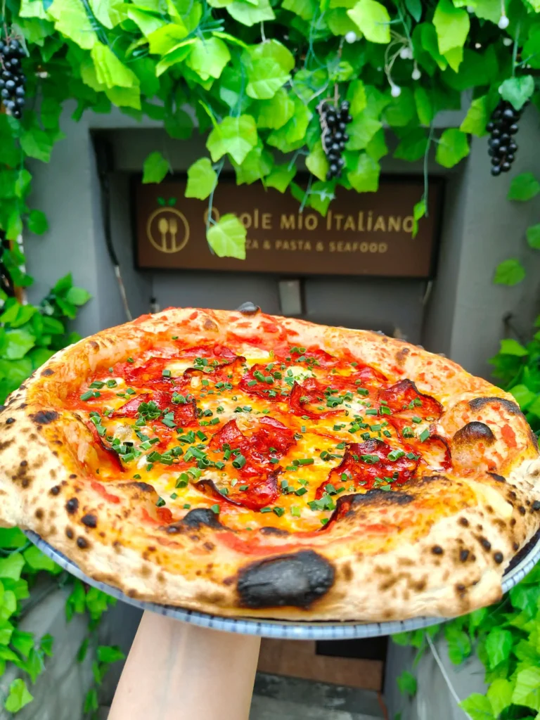 Pizza Picante ze spianatą pikantną i szczypiorkiem, trzymana przed wejściem do restauracji O Sole Mio Italiano
