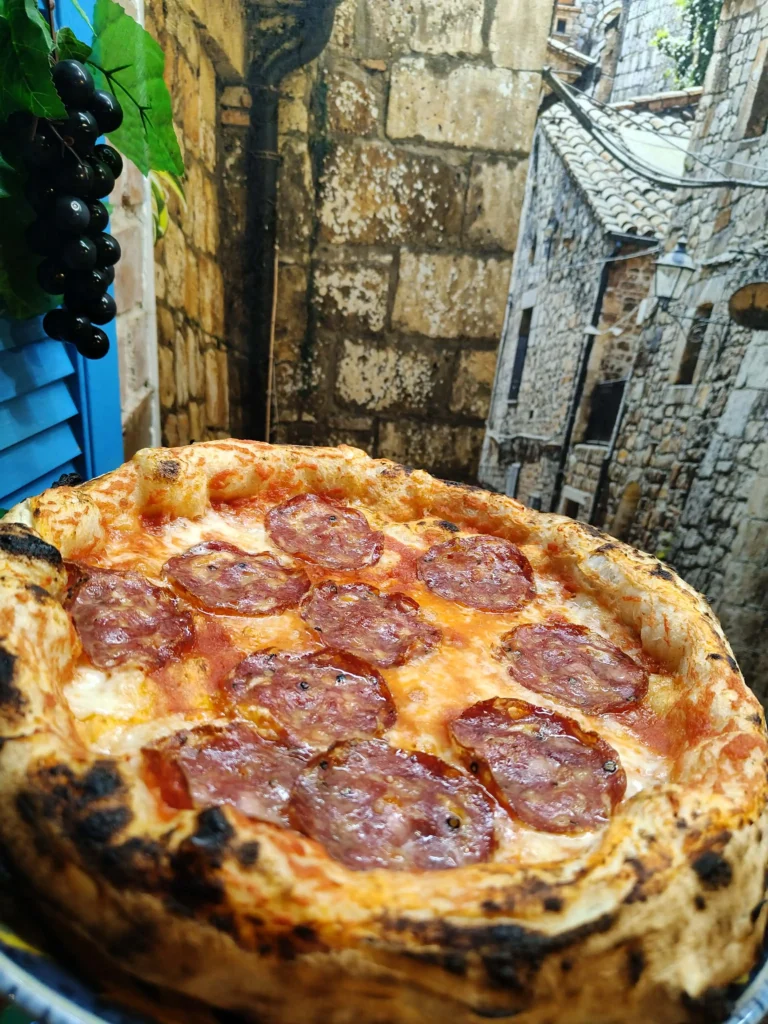 Pizza Salami Napoli z plastrami salami i mozzarellą, z widoczną leopardową skórką rantu
